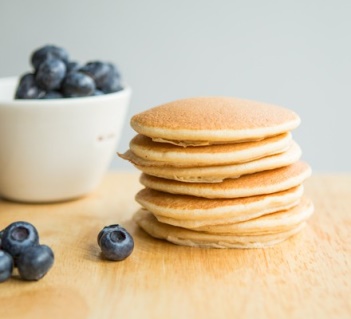 Stack of American pancakes on table with blueberries in bowl