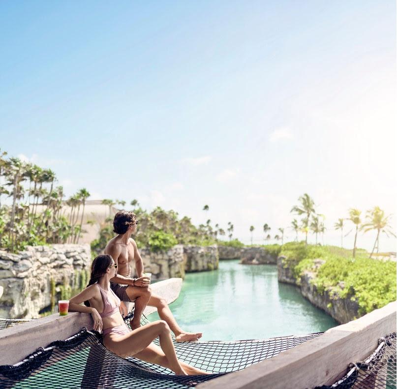 A group of people sitting on a hammock over a pool Description automatically generated