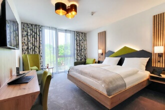 Modern bedroom with a large bed, green color accents, bedside tables, desk, chair and large windows with curtains.