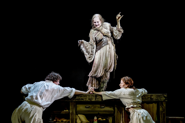 The Witch stands above the Baker and his Wife in a dramatic scene from Into the Woods