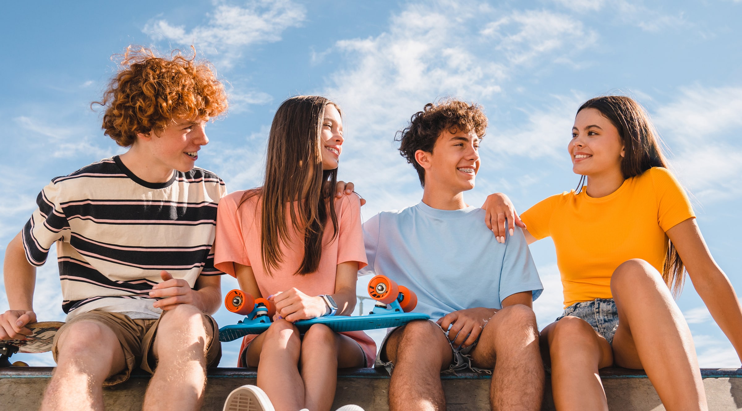 Group of friends sitting together outdoors with skateboards on a sunny day