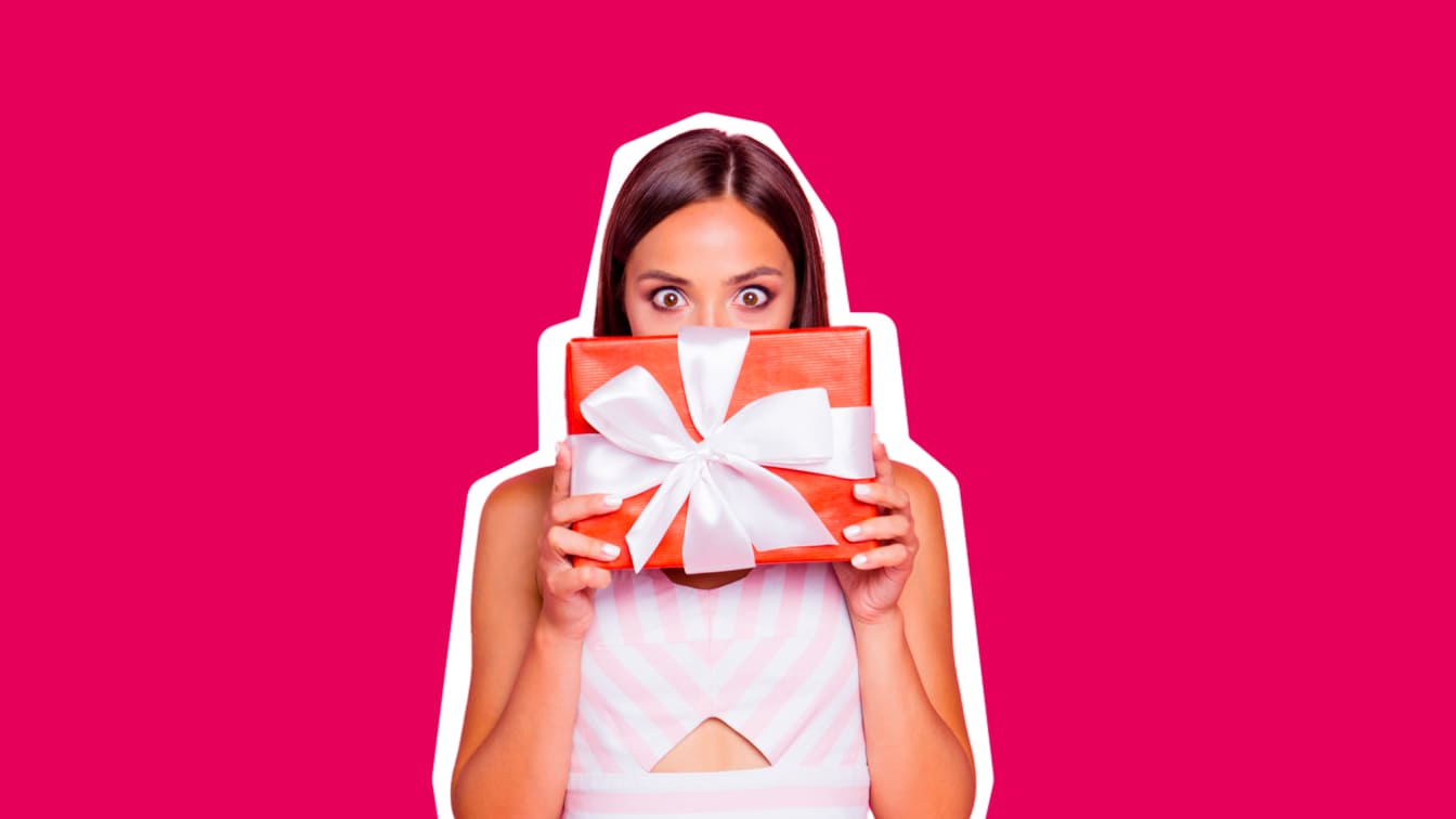 Smiling woman holding a wrapped gift on a pink background, from Enel's ENELtiPREMIA points collection programme