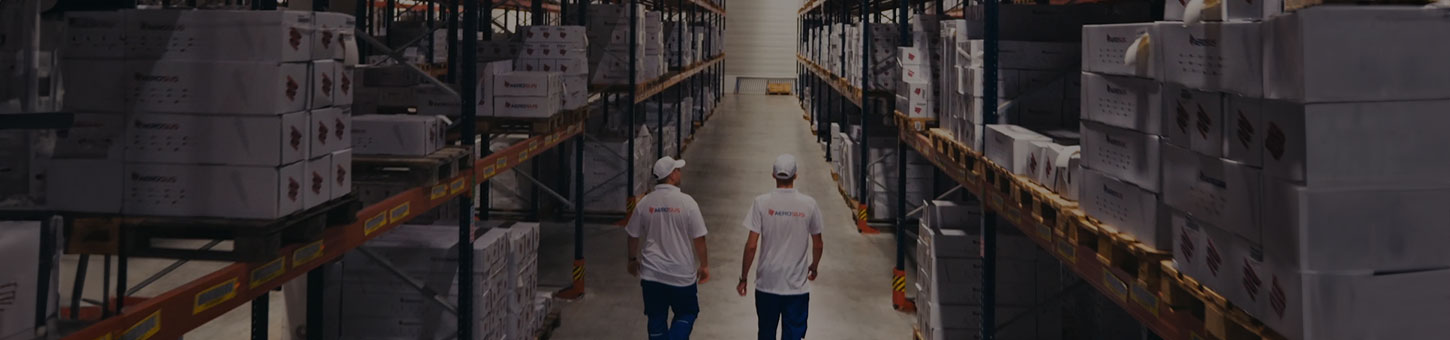 Two people walking through a warehouse aisle stacked with boxed parts