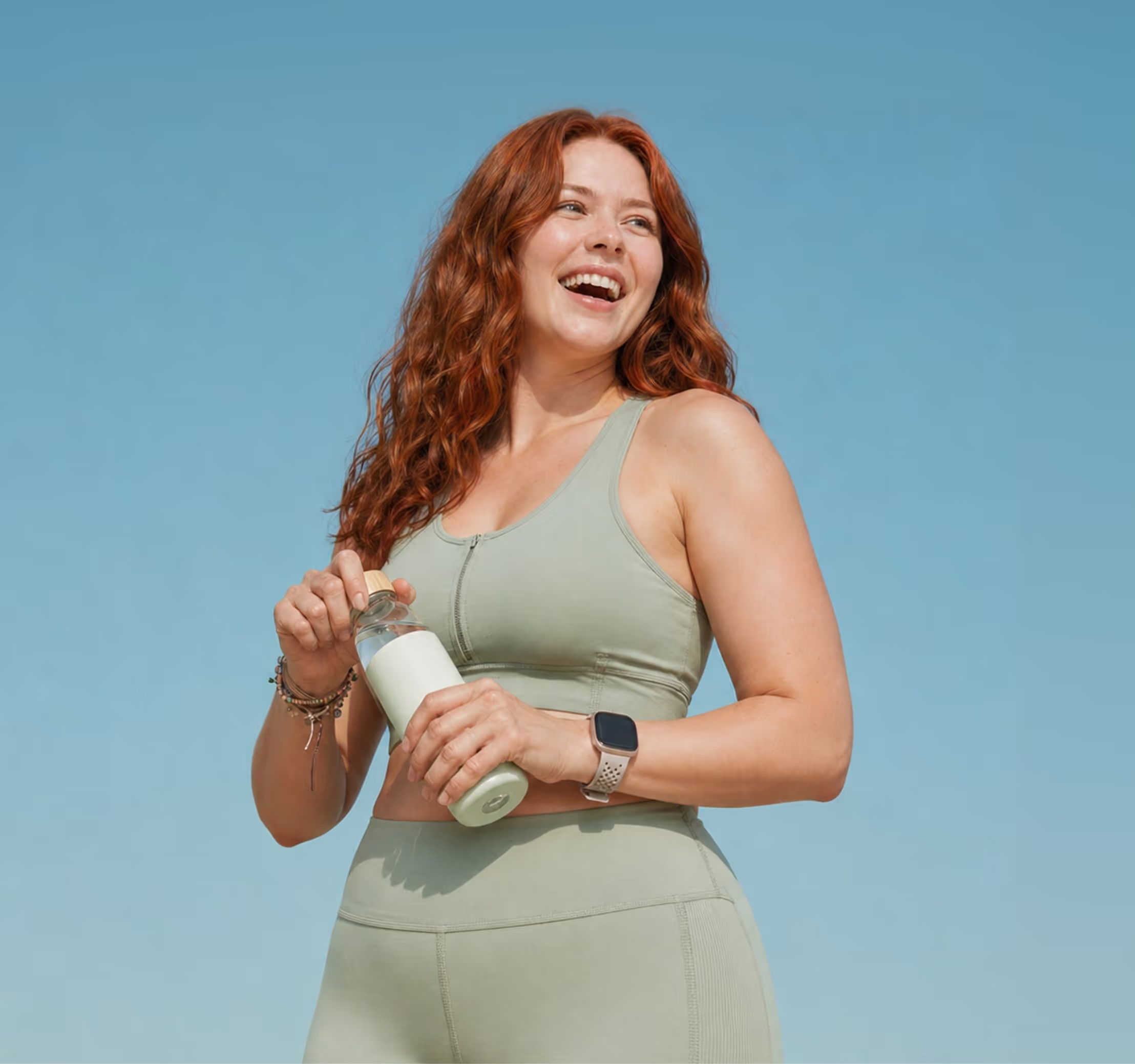 Smiling woman in activewear holding a water bottle outdoors