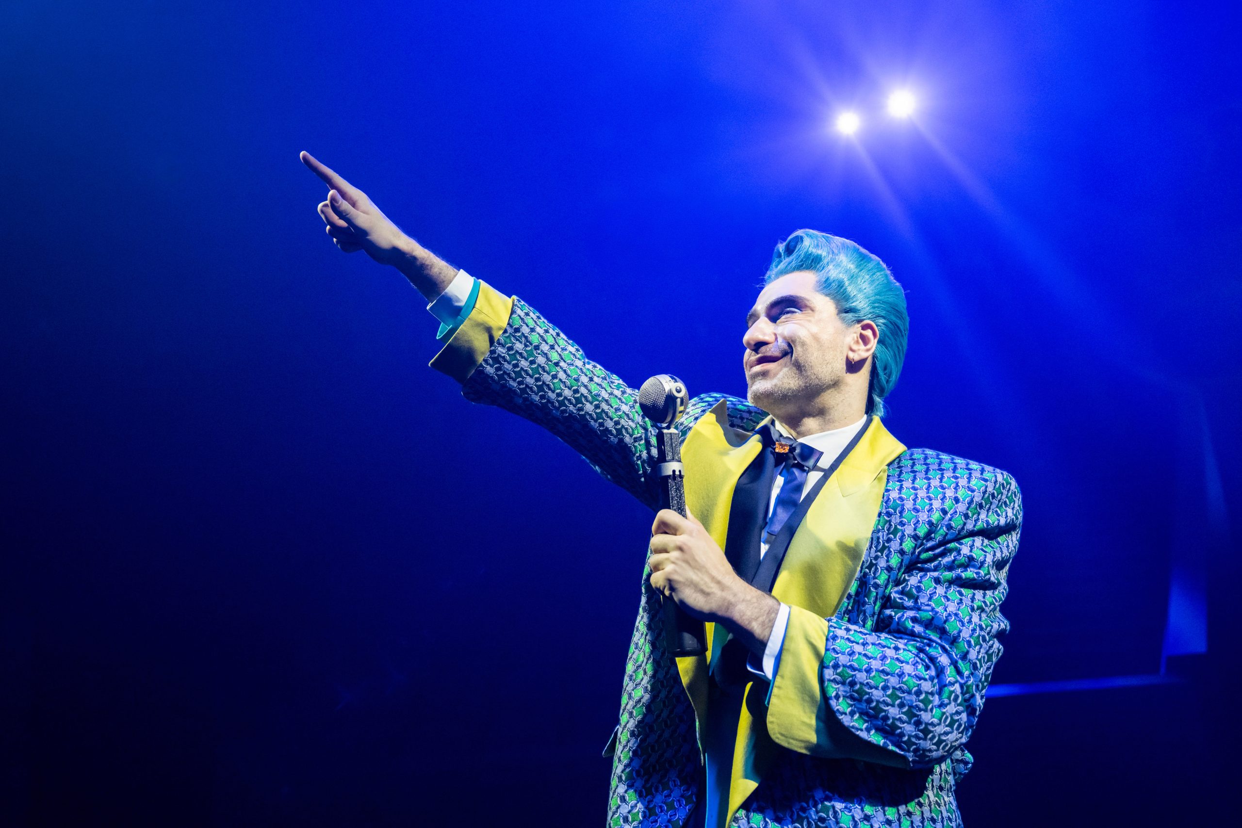A Capitol host with a microphone addresses the audience in The Hunger Games: On Stage