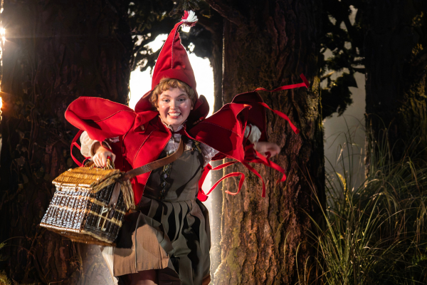 Little Red Ridinghood in her red cloak among the trees in Into the Woods