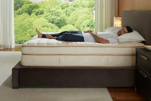 Person relaxing on a Saatva Classic mattress beside a large window