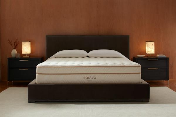 Saatva Classic made up with white bedding on a dark bed frame between two bedside lamps