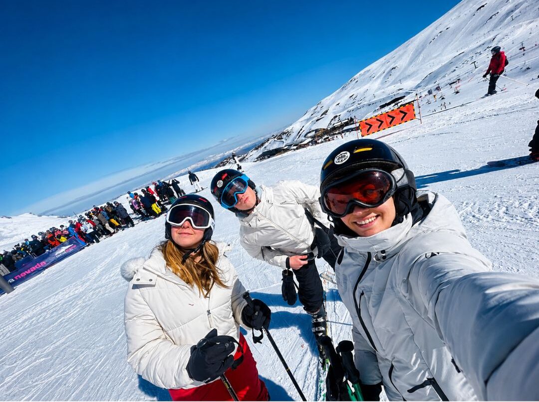 Students taking a selfie in ski gear on a sunny snowy slope