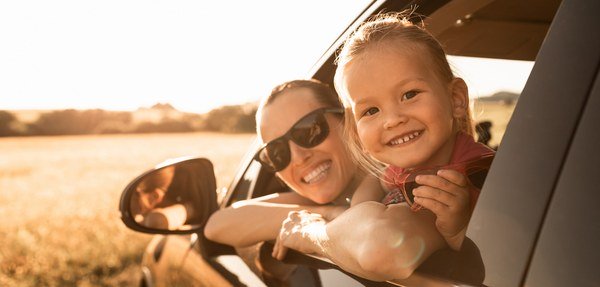Two children smiling in the back seat of a car on a road trip